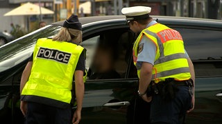 Eine französische Polizistin und ein deutscher Polizist kontrollieren gemeinsam den Fahrer eines schwarzen Autos.