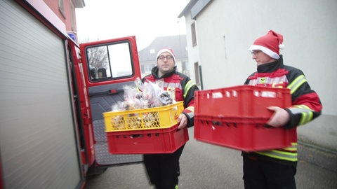 Zwei Männer in Feuerwehrkleidung mit Tüten voller Plätzchen  - die Feuerwehr Norsingen liefert selbstgebackene Plätzchen aus