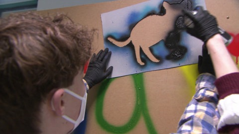Graffiti-Katzen in Schliengen: Ein Junge sprayt mit einer Schablone die Silhouette einer Katze.