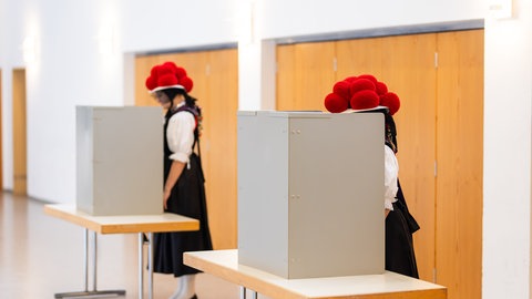 Zwei junge Frauen stehen in traditioneller Schwarzwälder Tracht mit Bollenhut in der Wahlkabine.