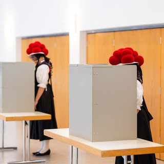 Zwei junge Frauen stehen in traditioneller Schwarzwälder Tracht mit Bollenhut in der Wahlkabine.
