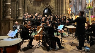 Sängerinnen und Sänger stehen neben dem Altar im Freiburger Münster. Sie tragen schwarz.