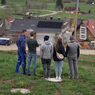 Die Waldauer Bauherren und Baufrau betrachten ihre Straße vom Berg aus.