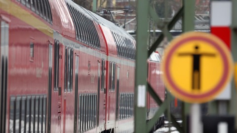 Ein Zug fährt in einem Bahnhof ein. Im Vordergrund ein Warnschild mit einem Menschen darauf. 