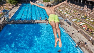 Mann spring vom Sprungturm ins Freibad-Becken. 