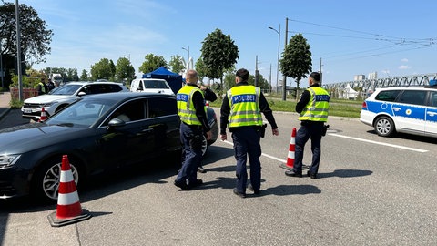 Drei Polizisten kontrollieren einen PKW, der am Straßenrand parkt