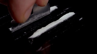 Weißes Kokainpulver wird auf einem schwarzen Untergrund zu einer Linie zusammengeschoben.