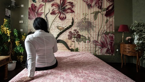 Eine Frau von hinten, die in einem Schlafzimmer auf dem Bett sitzt