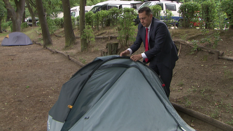 Bundestagsabgeordneter Johannes Fechner steht im Anzug auf dem Campingplatz und baut sein Ein-Mann-Zelt zusammen.