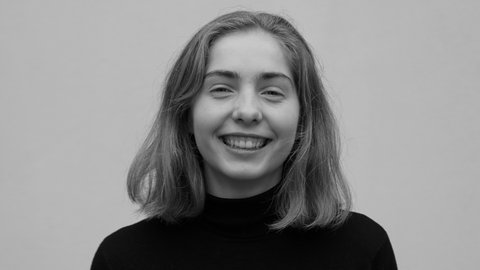 Frau mit schulterlangem Haar lächelt in die Kamera. Sie trägt einen schwarzen Pullover. das Bild ist schwarz-weiß eingefärbt.