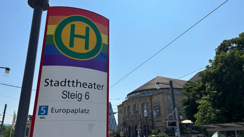 Das Haltestellenschild am Stadttheater in der Freiburger Innenstadt ist in Regenbogenfarben gehalten.