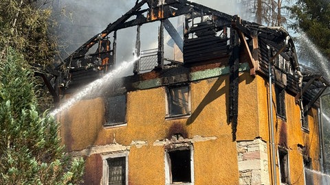 Feuerwehrleute bei einem brennenden Haus im Wald