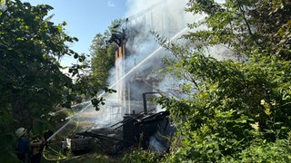 Löscharbeiten an einem brennenden Haus im Wald
