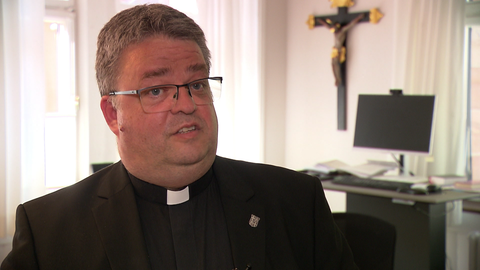 Generalvikar Christoph Neubrand sitzt am Schreibtisch in seinem Büro. Er verweist unter anderem auf geltendes Kirchenrecht.