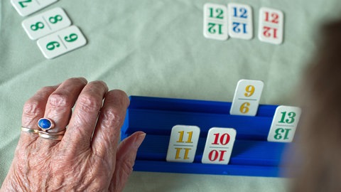 Auf dem Bild ist die linke Hand einer an Demenz erkrankten älteren Frau zu sehen, die das Denkspiel Rummikub spielt. Es handelt sich um ein Archivbild.