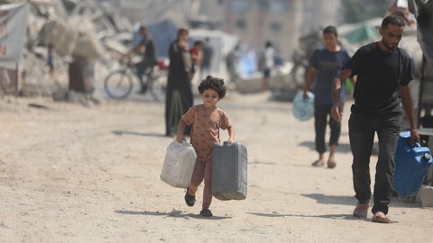 Ein Kind in Gaza trägt Wasserkanister.