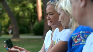 Ukrainische Frauen gucken sich am Handy Berichte über das Treffen von Trump und Putin an.