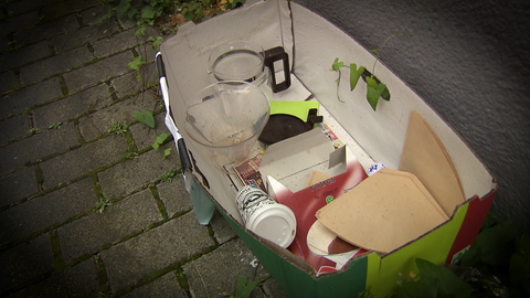 In einem Karton auf der Straße befinden sich verschiedene gebrauchte Kaffeeuntensilien. 