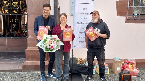 Oberbürgermeister Martin Horn (links) und Verkäufersprecher Karsten Koeleman mit der Käuferin der millionsten Ausgabe der Straßenzeitung "FREIeBÜRGER"