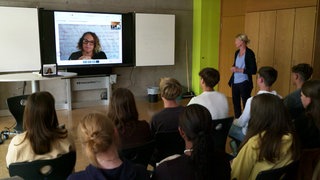 Lehrerin Simone Staritz (rechts stehend) moderiert das Gespräch ihrer Klasse mit der per Video zugeschalteten Expertin.