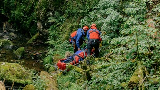 Zwei Personen der Bergwacht transportieren eine Person auf einer Bahre.