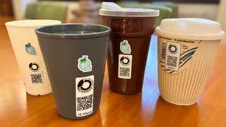 In einer Freiburger Bäckerei hängt ein Label mit einem Mehrweg-Symbol auf wiederverwendbaren Bechern.