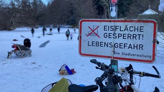 Der zugefrorene Waldsee in Freiburg. Viele Menschen laufen Schlittschuh auf der Eisfläche, obwohl Lebensgefahr besteht.