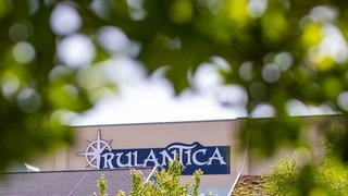 Zwischen Blättern lugt ein Stück einer Gebäudefassade hervor mit der Aufschrift "Rulantica".