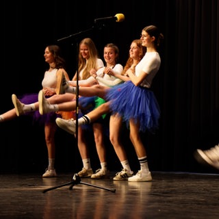 Mehrere Frauen in bunten Röcken auf einer Bühne. 