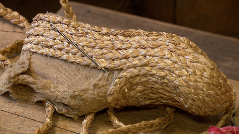 Ein Roggenstrohzopf wird mit einem Faden auf die Schuhleiste genäht. 