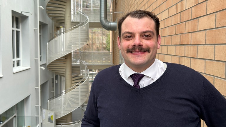 Ein Mann mit Schnurrbart lächelt in die Kamera.