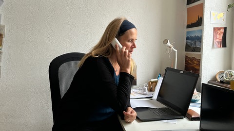 Sarah Pohl sitzt an einem Tisch und hält ein Telefon in der Hand. Das Bild zeigt sie von der Seite.