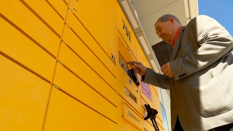 Ein Mann tippt auf das Display einer Poststation.