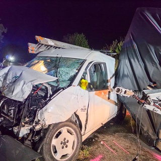 Ein Auto mit einem Anhänger stehen nach einem Unfall zerstört auf einer Straße.