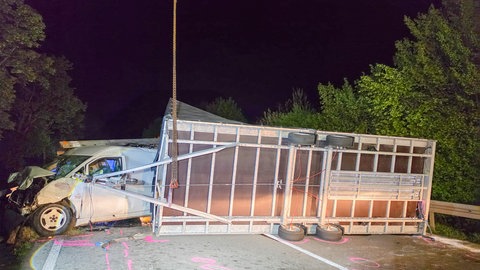 Ein Auto mit einem Anhänger stehen nach einem Unfall zerstört auf einer Straße.