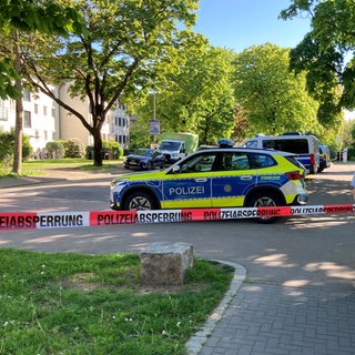 Polizisten und Anwohner hinter einem Absperrband in einem Wohnviertel