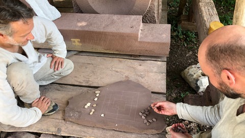 Mario und Julian spielen auf dem Campus Galli Mühle auf einem in Stein geritzten Spiel