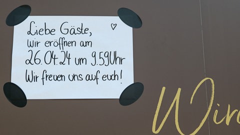 Lichtblick: Auf einem Schild steht: "Liebe Gäste, wir eröffnen am 26.04.24 um 9.59 Uhr. Wir freuen uns auf euch!"