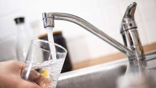 Ein Mann hält ein Glas unter einen laufenden Wasserhahn.