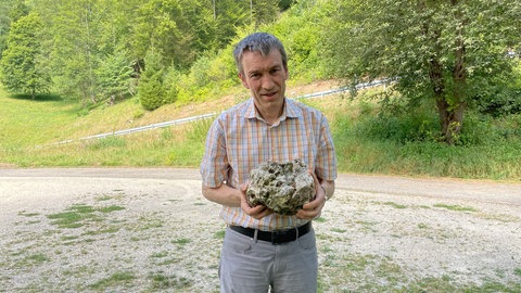 Helmuth Späth von der Bürgerinitiative "Keine Erweiterung Kernzone" hat einen Steinbrocken in der Hand, der einen Hang bei Schelklingen auf der Schwäbischen Alb hinabgerollt ist. 