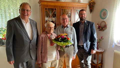 Im Wohnzimmer der Familie März in Betzingen stehen ein lachender Oberbürgermeister, ein zufriedener Bezirksbürgermeister und mit Blumenstrauß das Gnadenhochzeits-Paar.
