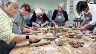 Beim Springerle-Backkurs in Münsingen stehen mehrere Frauen in grauen Schürzen am Tisch. Sie machen traditionelles Weihnachtsgebäck.