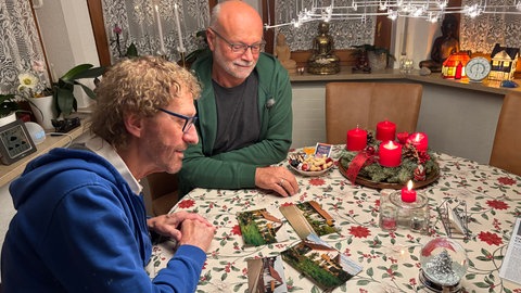 Zwei Männer sitzen am Küchentisch und sehen sich alte Fotos an, auf denen der Baum noch ganz klein war. Inzwischen soll er der schönste Weihnachtsbaum Tübingens sein.