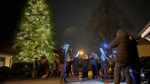 Der Lustnauer Posaunenchor spielt an einem Weihnachtsbaum im Freien. 