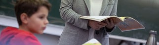 Schüler mit Lehrerin mit Buch in der Hand im Klassenzimmer: An Tübinger Schulen soll unter anderem an Schulsozialarbeit gespart werden wegen Schulden. Dagegen regt sich Protest.