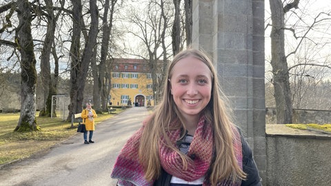 Lotta Brockel steht lächelnd in einigem Abstand vor dem gelben Gebäude mit den grünen Fensterläden. Als Jugendguide erklärt sie Besuchern die NS-Vergangenheit des Gebäudes.
