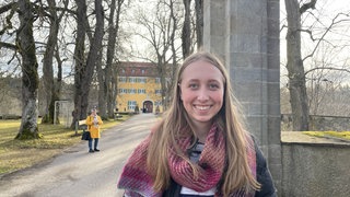 Lotta Brockel steht lächelnd in einigem Abstand vor dem gelben Gebäude mit den grünen Fensterläden. Als Jugendguide erklärt sie Besuchern die NS-Vergangenheit des Gebäudes.