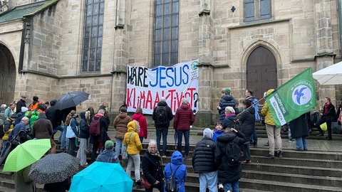 Obwohl es immer wieder geregnet hat, sind über 50 Menschen gekommen, um dabei zu sein, als bei Musik und Applaus das Banner an der Stiftskirche in Tübingen abgerollt wurde.