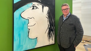 Bernd Feil, Geschäftsführer und Kurator des Neuen Kunstmuseums Tübingen, neben einem Selbstporträt von Udo Lindenberg. Erste Ausstellung, Panik in Tübingen, Bilder von Udo Lindenberg.