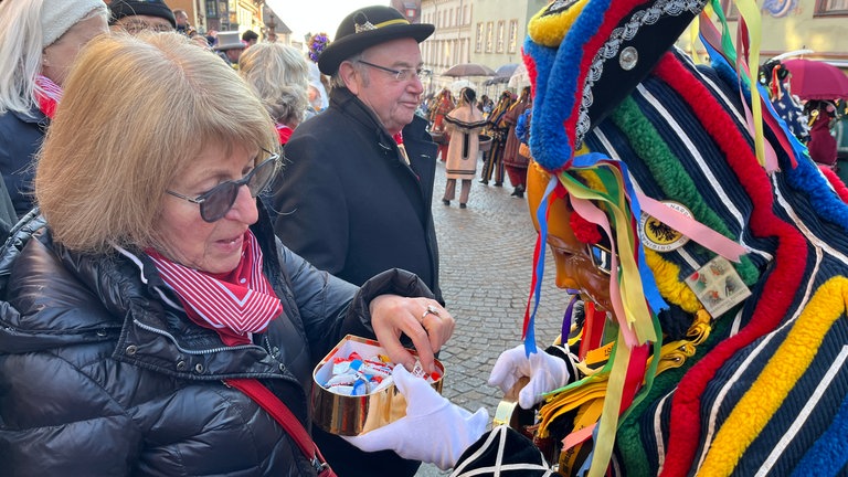 Eine Frau bekommt von einem Narr etwas zum Naschen beim Narrensprung in Rottweil
